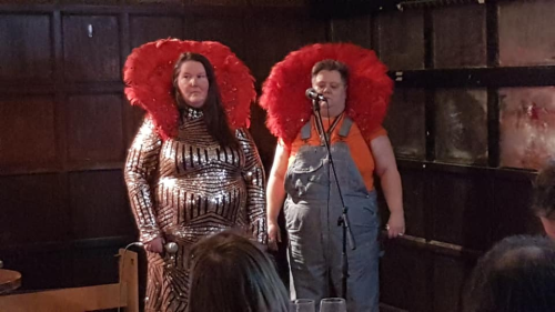 Homosexual Death Drive with feathers, sequins, dungarees, looking sideways